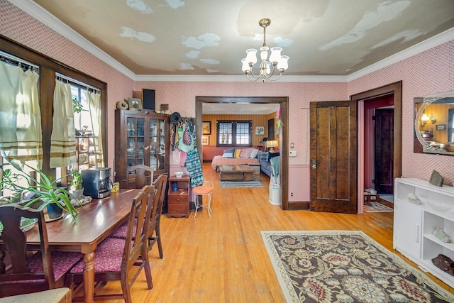 dining room with light wood finished floors, a notable chandelier, wallpapered walls, and crown molding