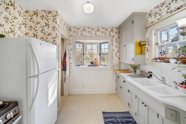 kitchen with a sink, baseboards, a healthy amount of sunlight, and freestanding refrigerator