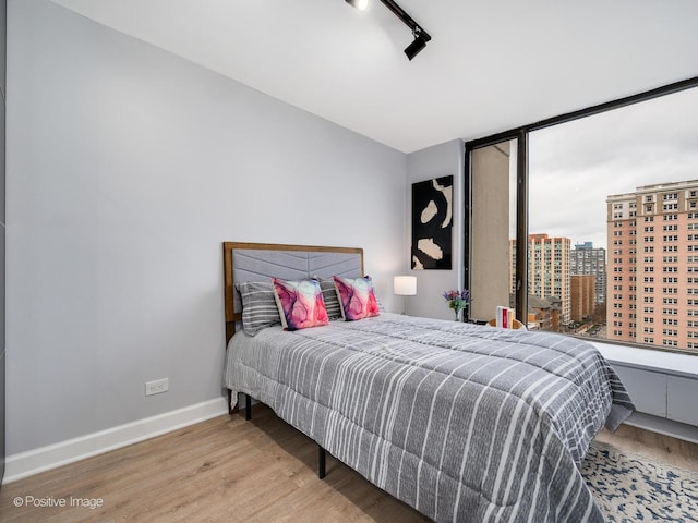 bedroom with track lighting, wood finished floors, and baseboards