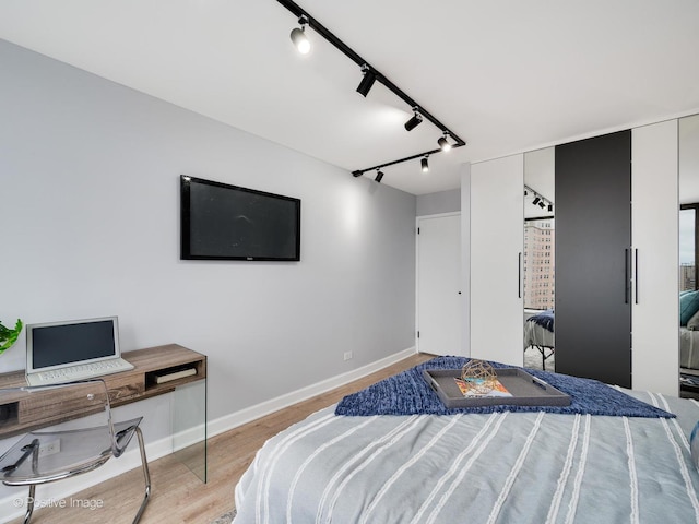 bedroom with track lighting, baseboards, and light wood-type flooring