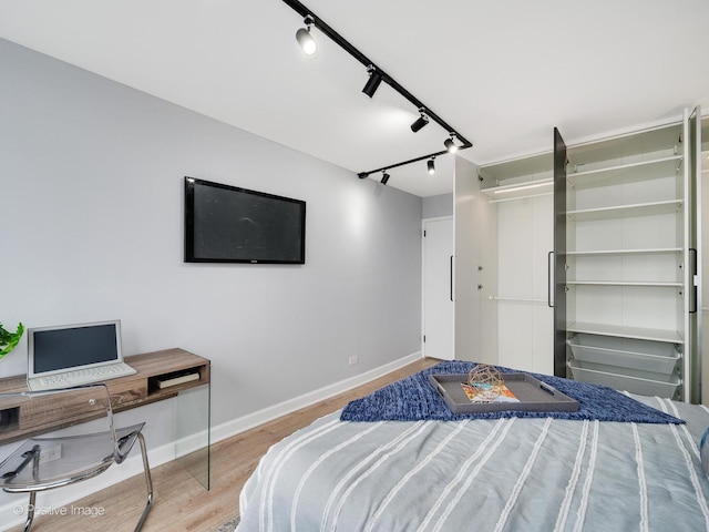 bedroom with rail lighting, wood finished floors, and baseboards