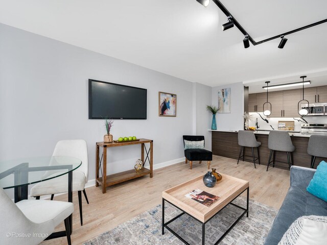 living room with track lighting, baseboards, and light wood-type flooring