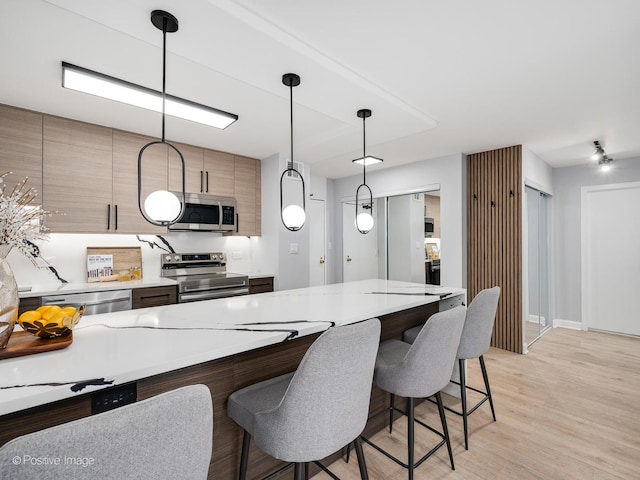 kitchen featuring light countertops, light wood-style flooring, a kitchen breakfast bar, stainless steel appliances, and modern cabinets