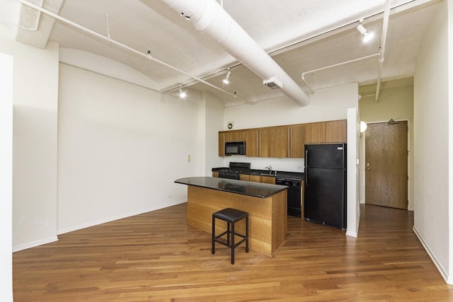 kitchen featuring dark countertops, brown cabinets, rail lighting, wood finished floors, and black appliances