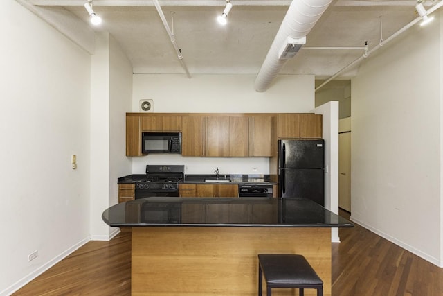 kitchen with black appliances, track lighting, a sink, dark countertops, and dark wood-style flooring
