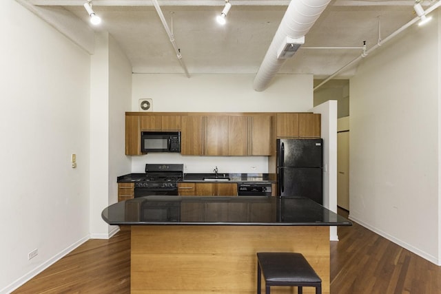 kitchen featuring dark countertops, dark wood finished floors, black appliances, and a sink