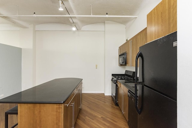 kitchen featuring dark countertops, track lighting, a center island, dark wood-style floors, and black appliances