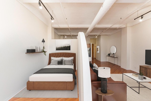 bedroom featuring rail lighting, wood finished floors, and baseboards
