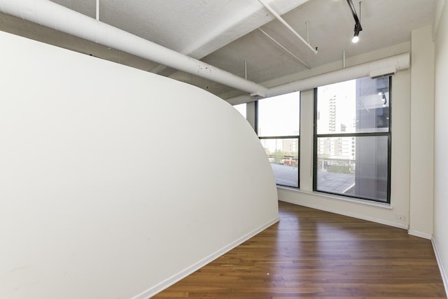 unfurnished room featuring baseboards, wood finished floors, and rail lighting