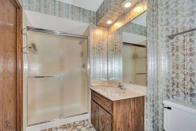 bathroom featuring wallpapered walls, a shower stall, toilet, and vanity