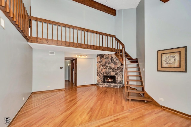 unfurnished living room featuring beam ceiling, stairway, light wood-style flooring, and visible vents