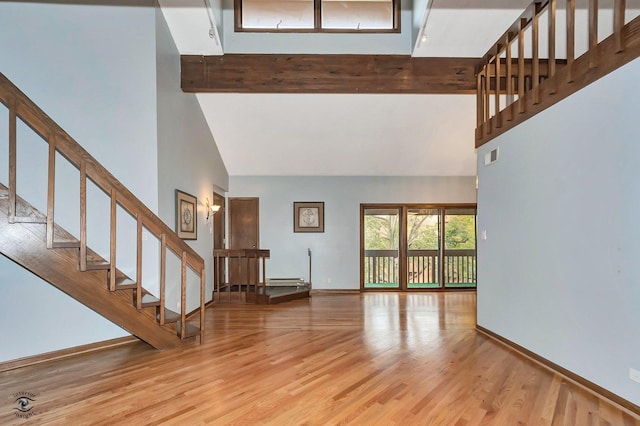 unfurnished living room with beamed ceiling, wood finished floors, and a towering ceiling