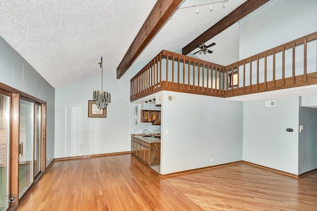 unfurnished living room with visible vents, baseboards, beamed ceiling, ceiling fan with notable chandelier, and light wood-style flooring