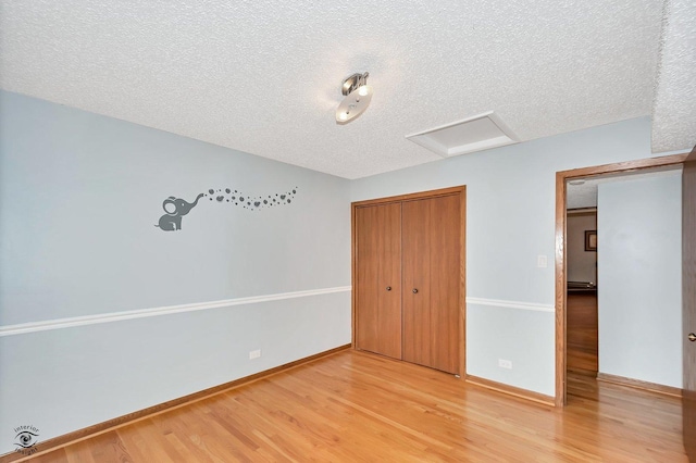 unfurnished bedroom with baseboards, attic access, light wood-style floors, a closet, and a textured ceiling