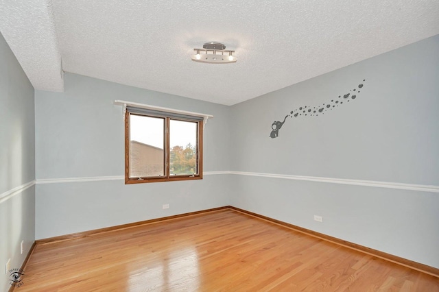 unfurnished room featuring baseboards, light wood-type flooring, and a textured ceiling