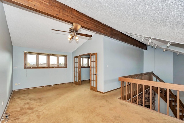 empty room with french doors, carpet floors, a textured ceiling, and vaulted ceiling with beams