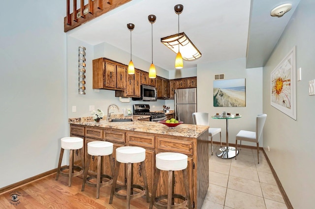 kitchen featuring visible vents, a sink, light stone counters, appliances with stainless steel finishes, and a peninsula