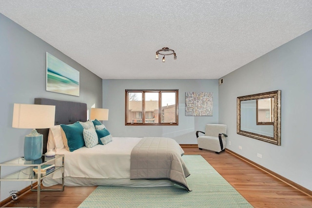 bedroom featuring a textured ceiling, baseboards, and wood finished floors