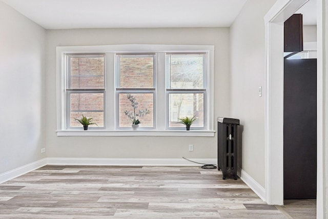 spare room featuring light wood-style flooring, radiator heating unit, and baseboards