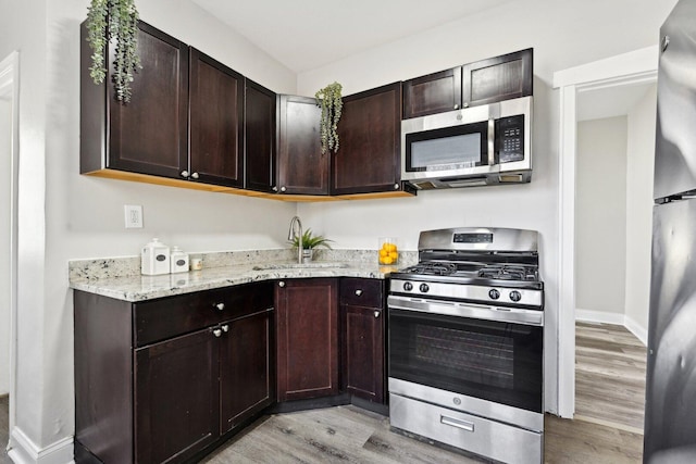 kitchen with light stone counters, light wood-style flooring, a sink, dark brown cabinetry, and appliances with stainless steel finishes