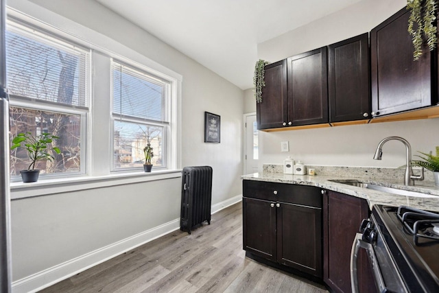 kitchen with range with gas stovetop, light stone counters, baseboards, light wood finished floors, and a sink