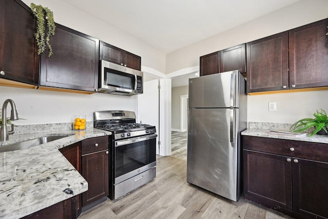 kitchen with dark brown cabinetry, light stone counters, light wood-style flooring, appliances with stainless steel finishes, and a sink