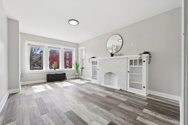 unfurnished living room featuring radiator, a fireplace, baseboards, and wood finished floors