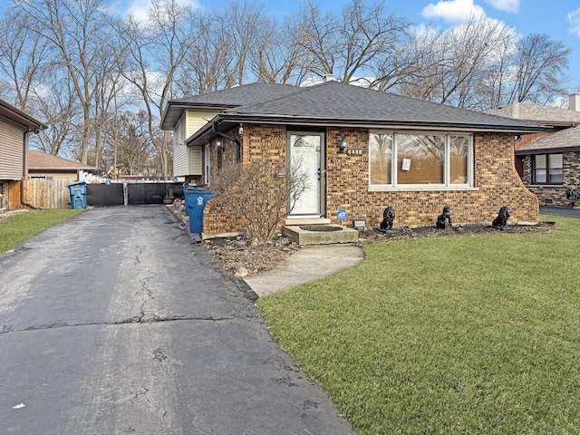 view of front of home with aphalt driveway, brick siding, a front lawn, and fence