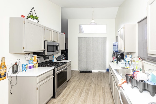 kitchen featuring pendant lighting, light countertops, light wood-style floors, stainless steel appliances, and a sink