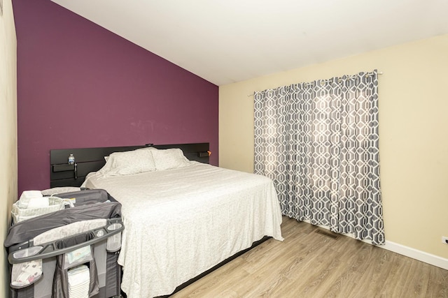 bedroom featuring visible vents, baseboards, light wood-style floors, and vaulted ceiling