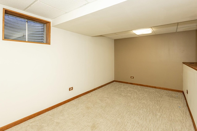 finished basement with a paneled ceiling, baseboards, and light carpet