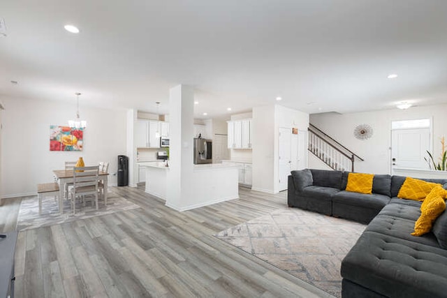 living room featuring baseboards, an inviting chandelier, light wood-style flooring, recessed lighting, and stairs