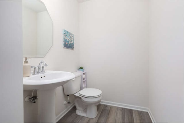 half bathroom featuring toilet, wood finished floors, and baseboards