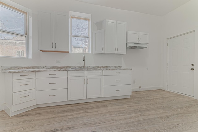 kitchen featuring a sink, baseboards, light wood-style flooring, and white cabinetry