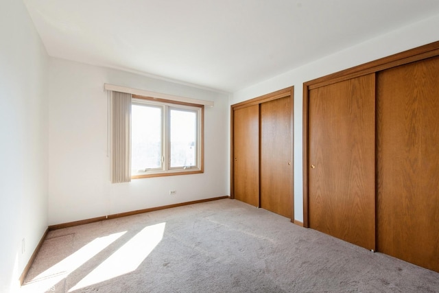 unfurnished bedroom featuring baseboards, two closets, and carpet