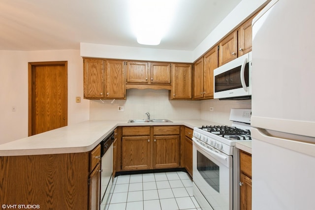 kitchen featuring white appliances, a peninsula, brown cabinets, and a sink