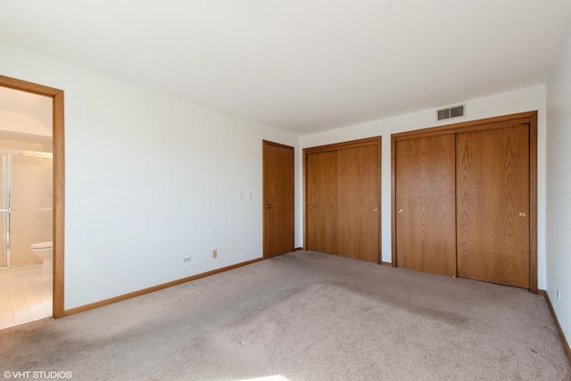 unfurnished bedroom featuring visible vents, two closets, baseboards, carpet floors, and ensuite bathroom