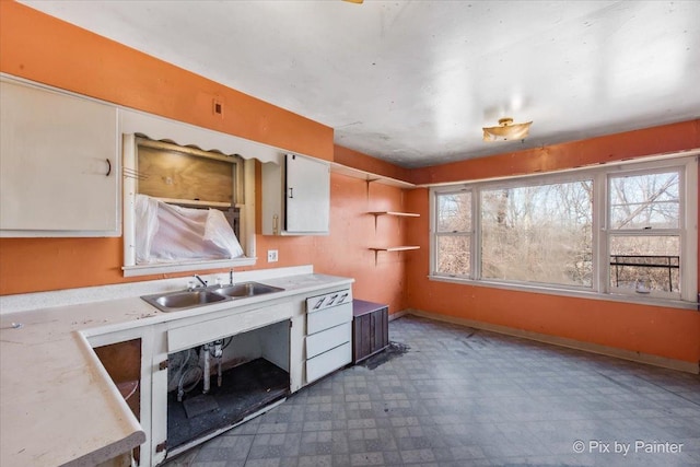 kitchen with tile patterned floors, a sink, white cabinets, light countertops, and baseboards