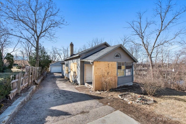 view of front of property with a chimney, a detached garage, an outdoor structure, and fence