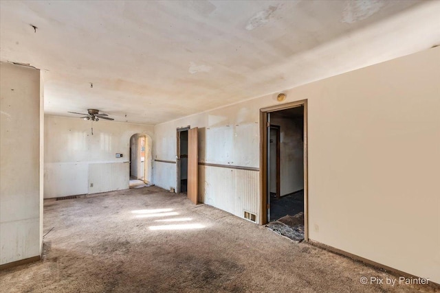 carpeted empty room featuring a ceiling fan and arched walkways