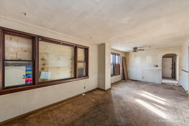 carpeted empty room featuring baseboards, arched walkways, and ceiling fan