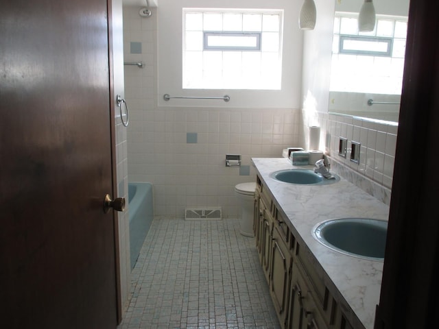 bathroom with visible vents, toilet, tile walls, and a sink