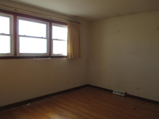 unfurnished room featuring visible vents, baseboards, and wood finished floors