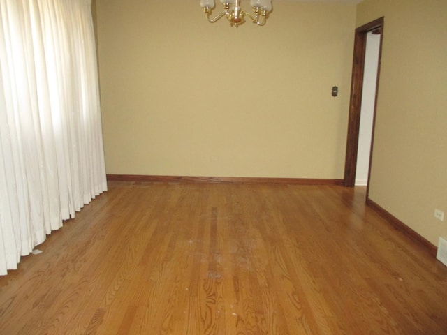 empty room with baseboards, light wood-type flooring, and a chandelier