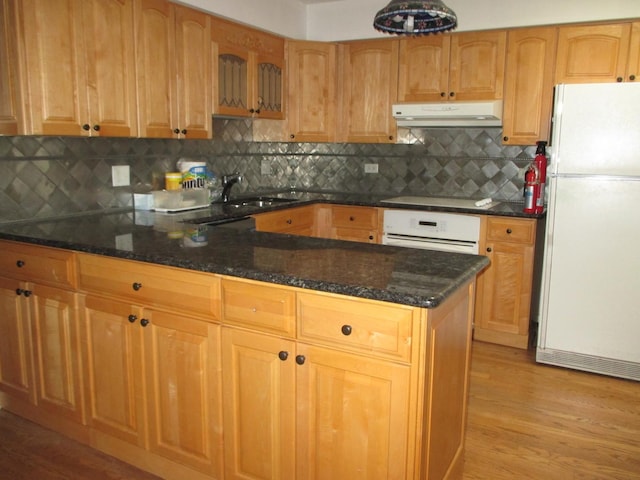 kitchen with under cabinet range hood, dark stone countertops, a peninsula, white appliances, and a sink