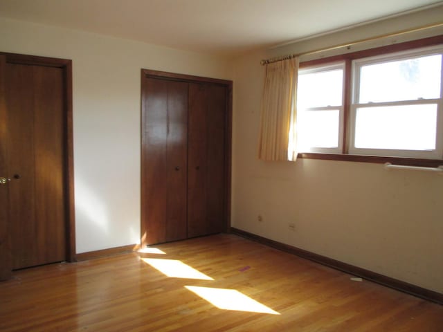 unfurnished bedroom with light wood-style floors, baseboards, and two closets