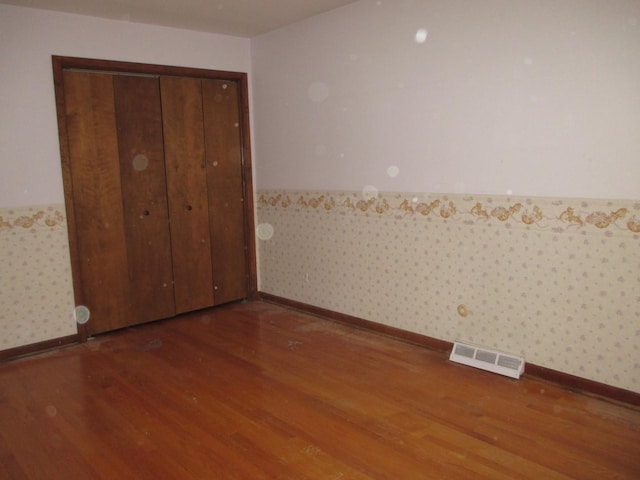 unfurnished bedroom featuring visible vents, wallpapered walls, wood finished floors, and a wainscoted wall