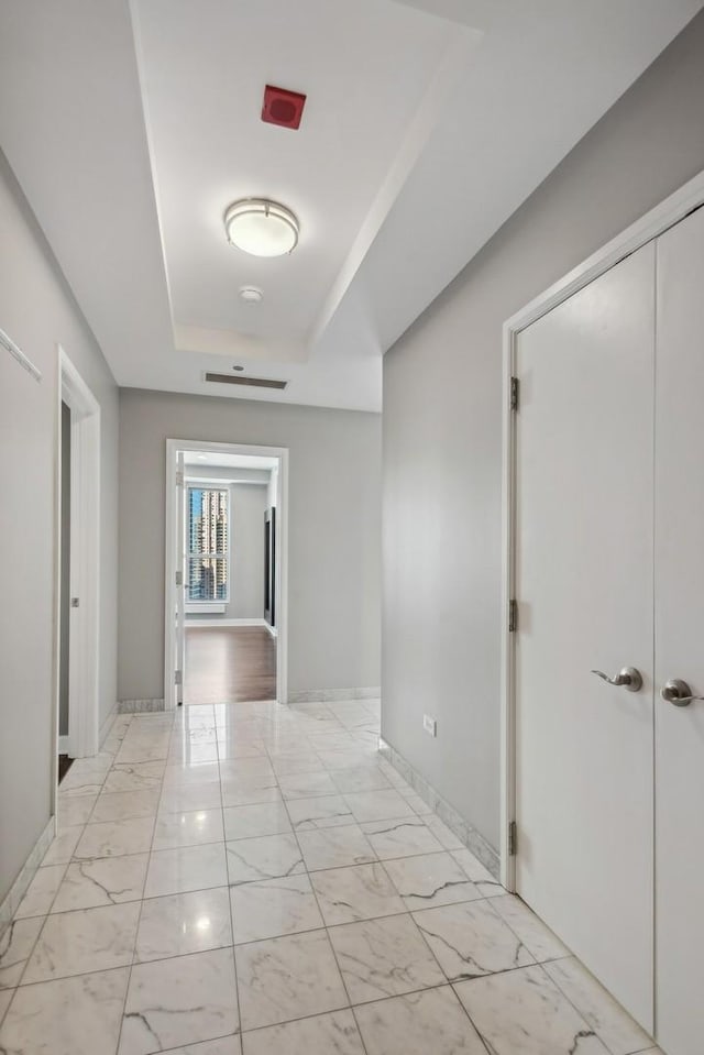 corridor featuring marble finish floor, a raised ceiling, and baseboards