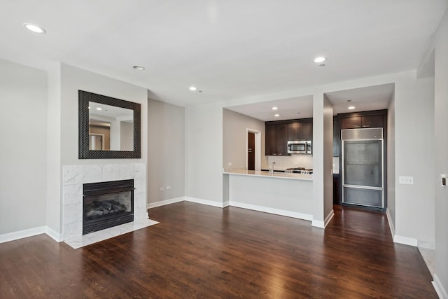 unfurnished living room featuring recessed lighting, baseboards, dark wood finished floors, and a high end fireplace