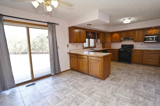 kitchen featuring black gas range oven, visible vents, a sink, under cabinet range hood, and stainless steel microwave